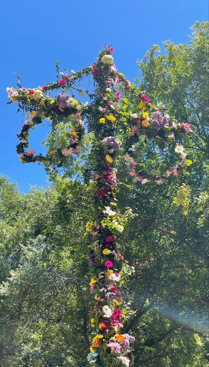 a cross made out of flowers and leaves in the middle of a field with trees behind it