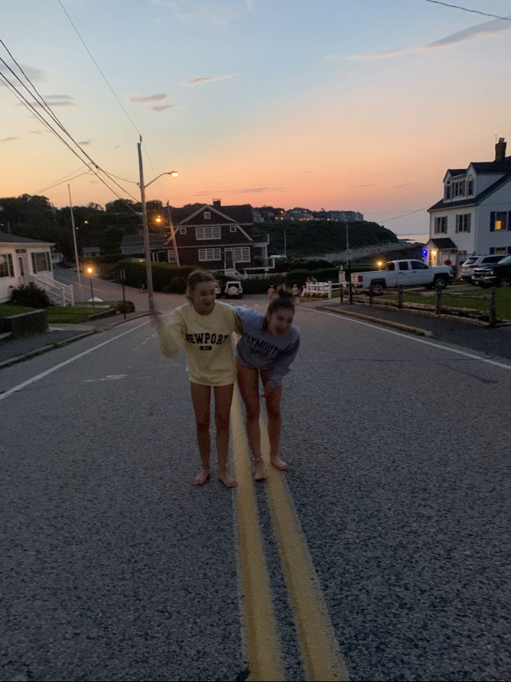 two girls are playing in the middle of the street at sunset with their arms around each other