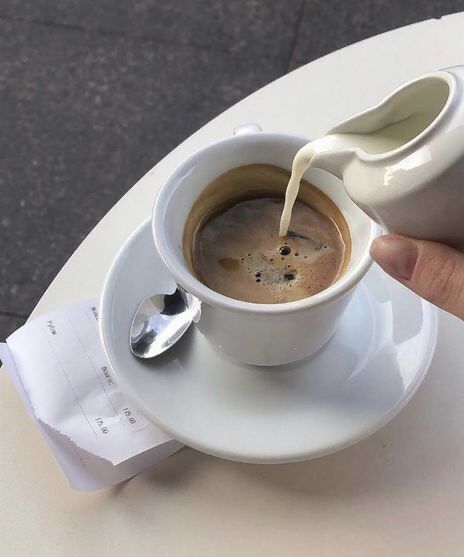 a person pouring milk into a cup on top of a white saucer and spoon