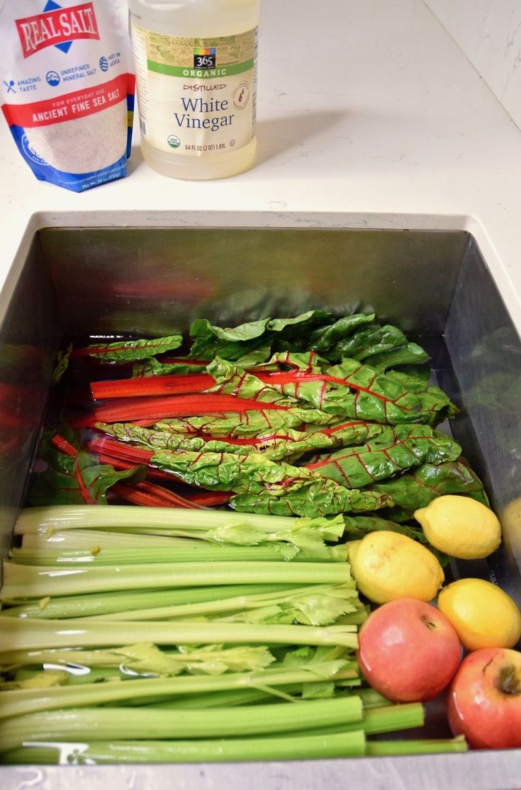 some vegetables are in a metal container on the counter next to an apple and water bottle