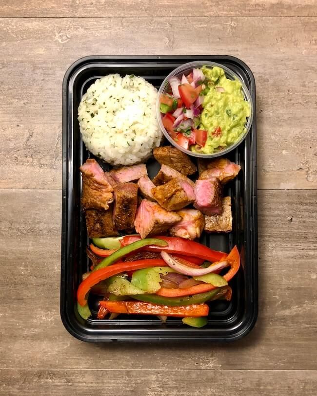 a tray filled with meat and vegetables on top of a wooden table next to rice