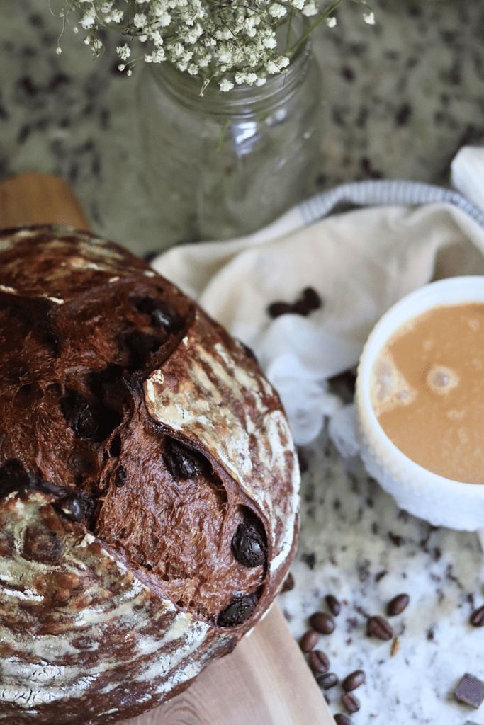 a loaf of bread sitting on top of a wooden cutting board next to a cup of coffee