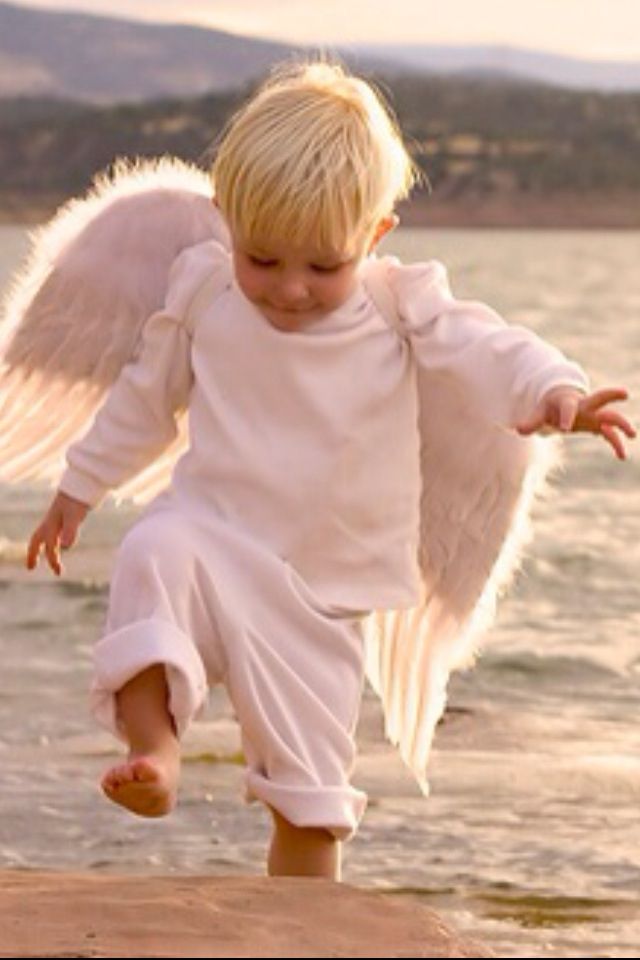 a little boy dressed up like an angel running on the beach with his wings spread