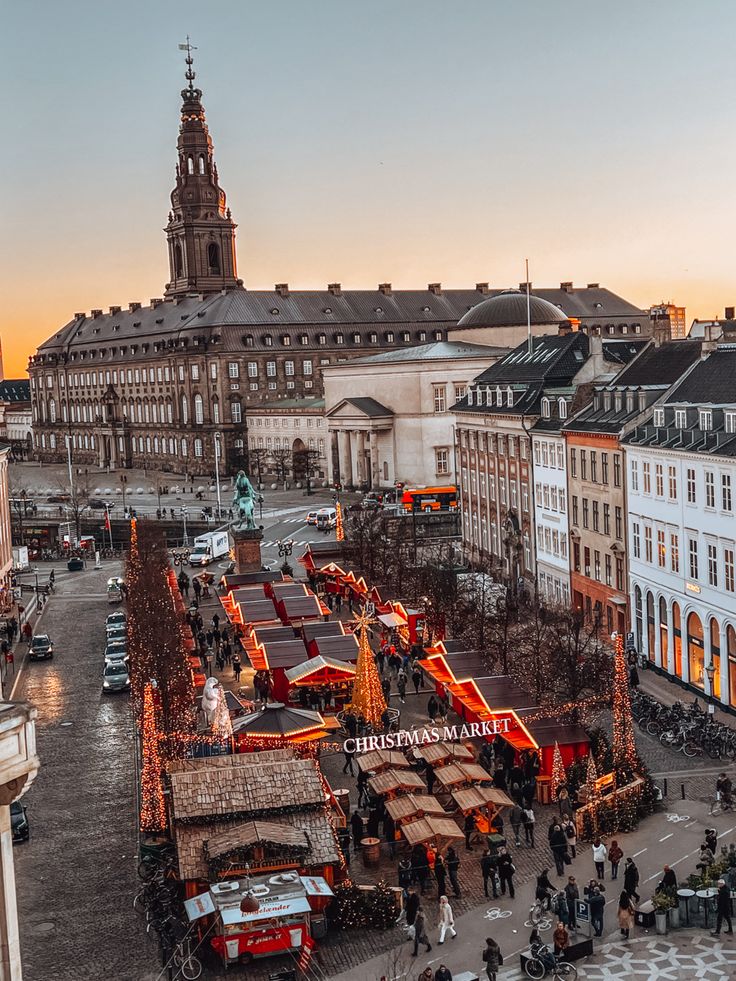 an aerial view of a christmas market in the middle of a city at dusk with people walking around