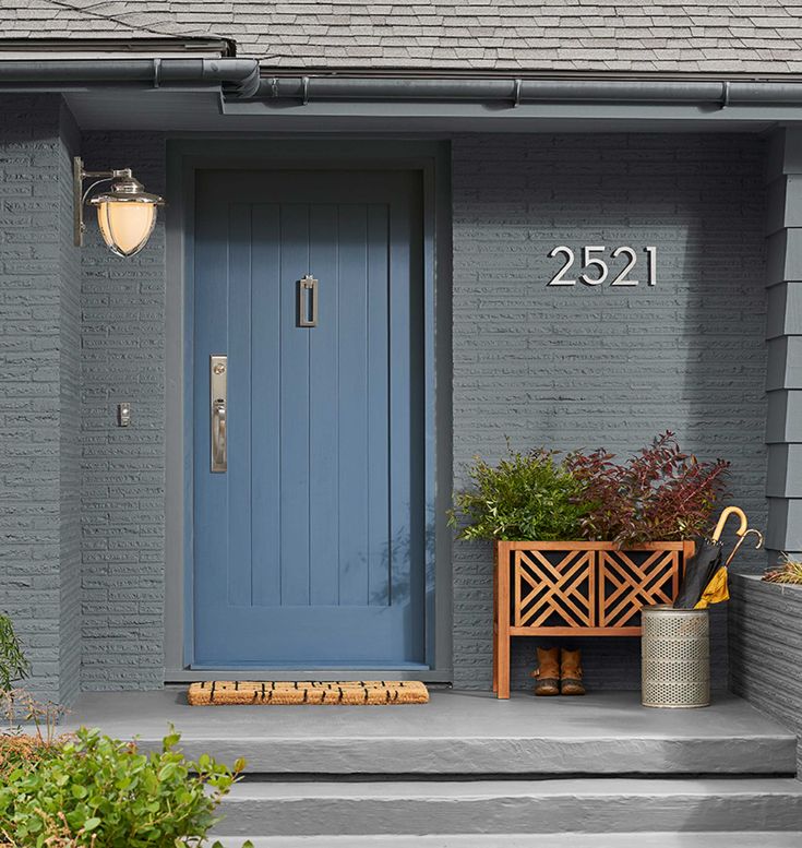 a blue front door on a gray house with potted plants in the foreground