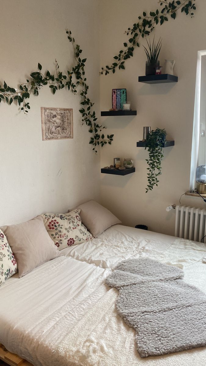 a bed with pillows, blankets and plants on the wall above it in a bedroom