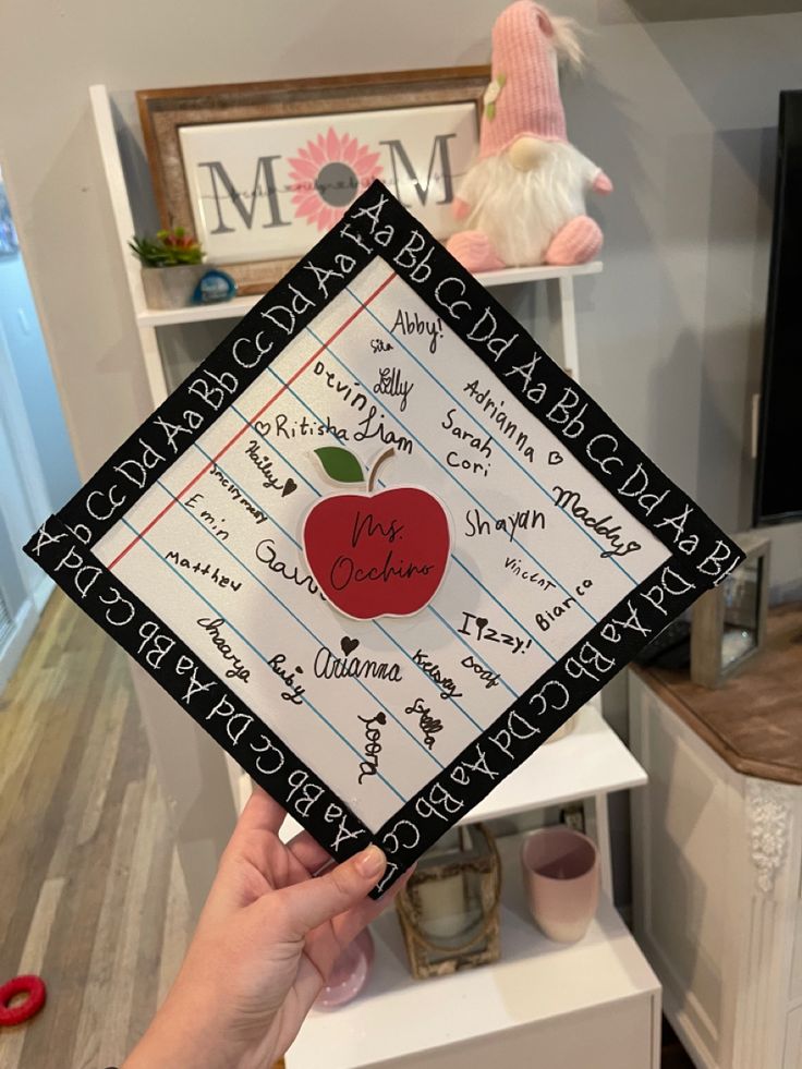 a person holding up a graduation cap with an apple on it and writing all over it