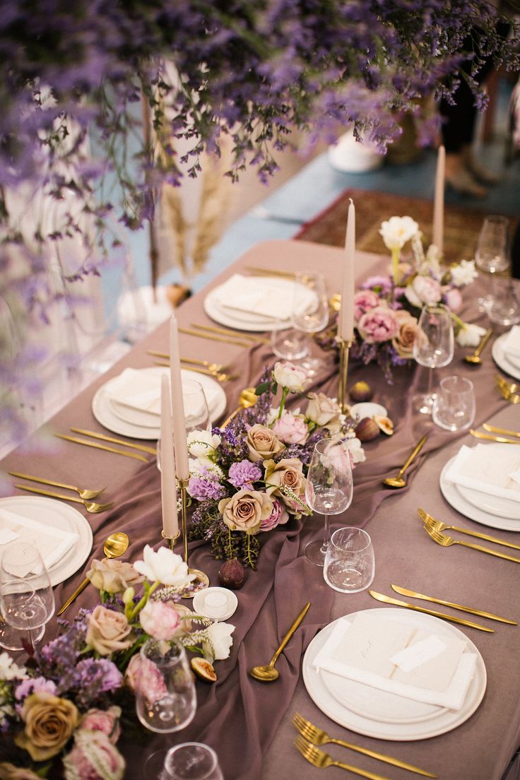 the table is set with white plates and purple napkins, silverware and flowers