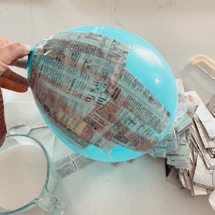 a person is holding a blue ball with newspaper on it next to a pile of newspapers