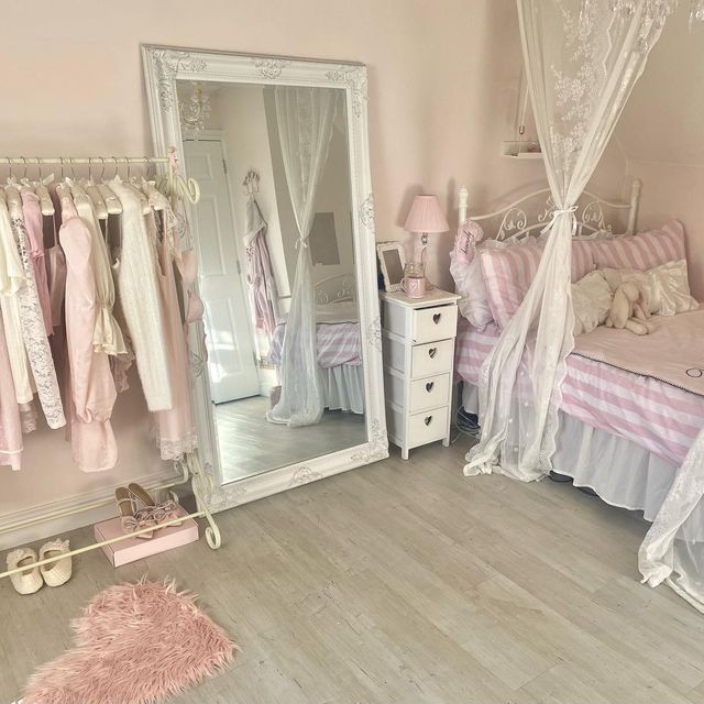 a bedroom with pink and white furniture and clothes hanging on the wall, including a large mirror