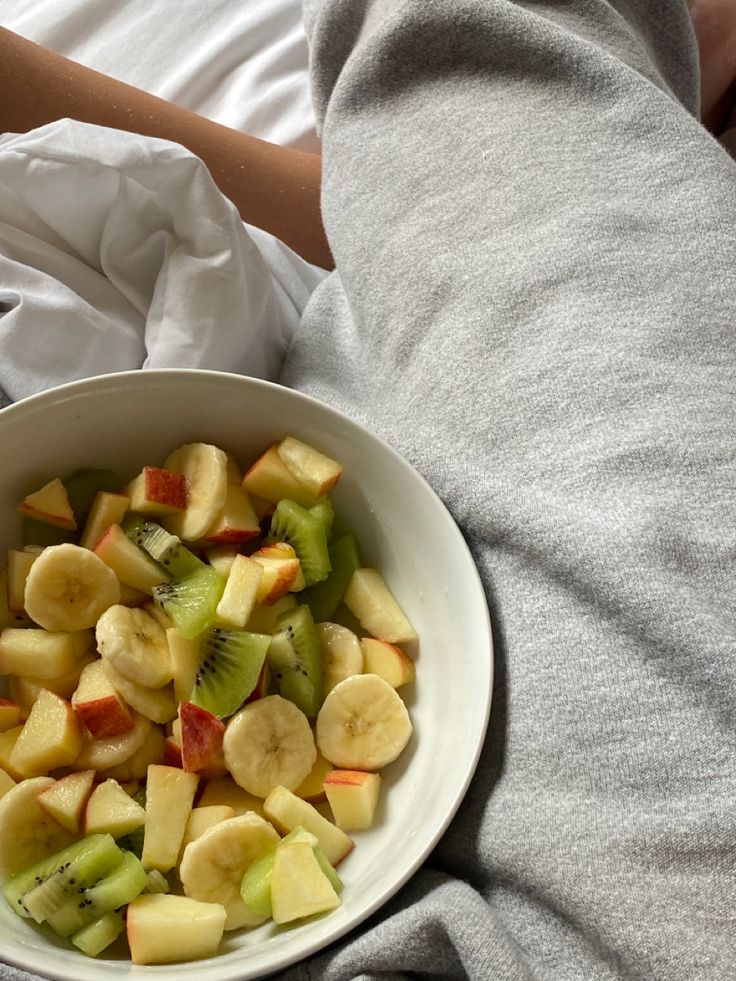 a white bowl filled with cut up fruit on top of a bed next to a person