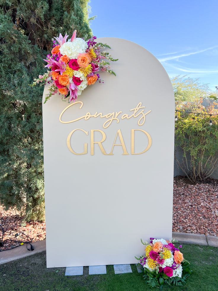 a sign that says congrats grad with flowers on it in front of some bushes