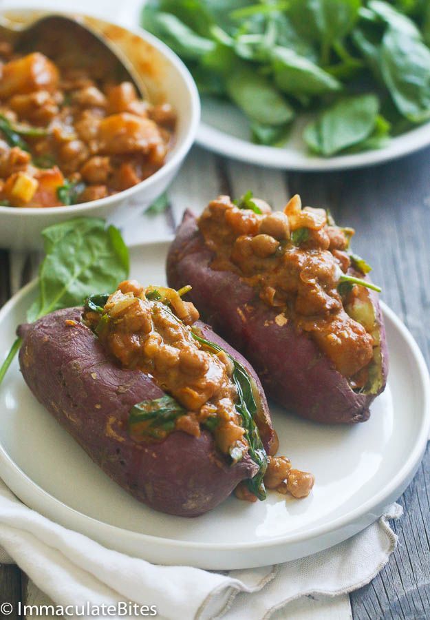 two stuffed sweet potatoes on a plate with spinach and other vegetables in the background