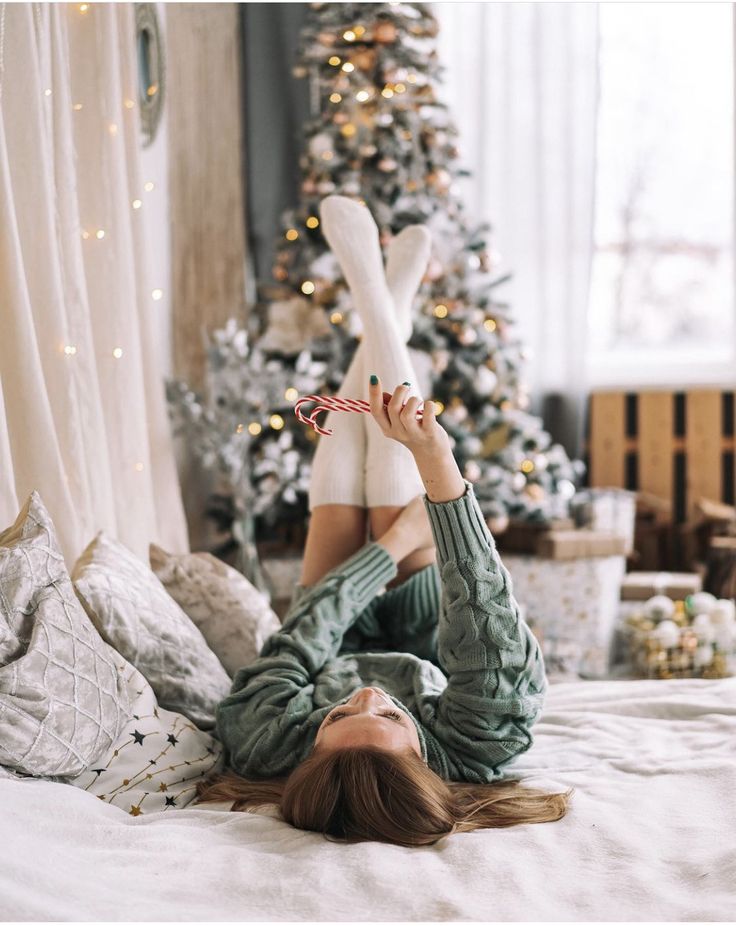 a woman laying on top of a bed in front of a christmas tree with her feet up