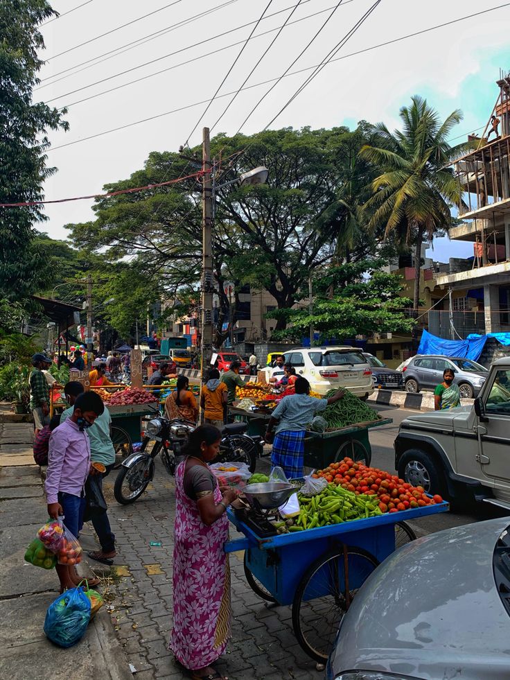 people are shopping at an outdoor market on the side of the road with cars and motorcycles