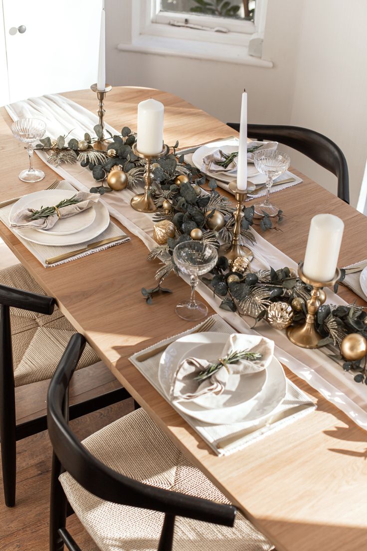 the table is set for christmas dinner with silver and gold decorations on it, along with candles