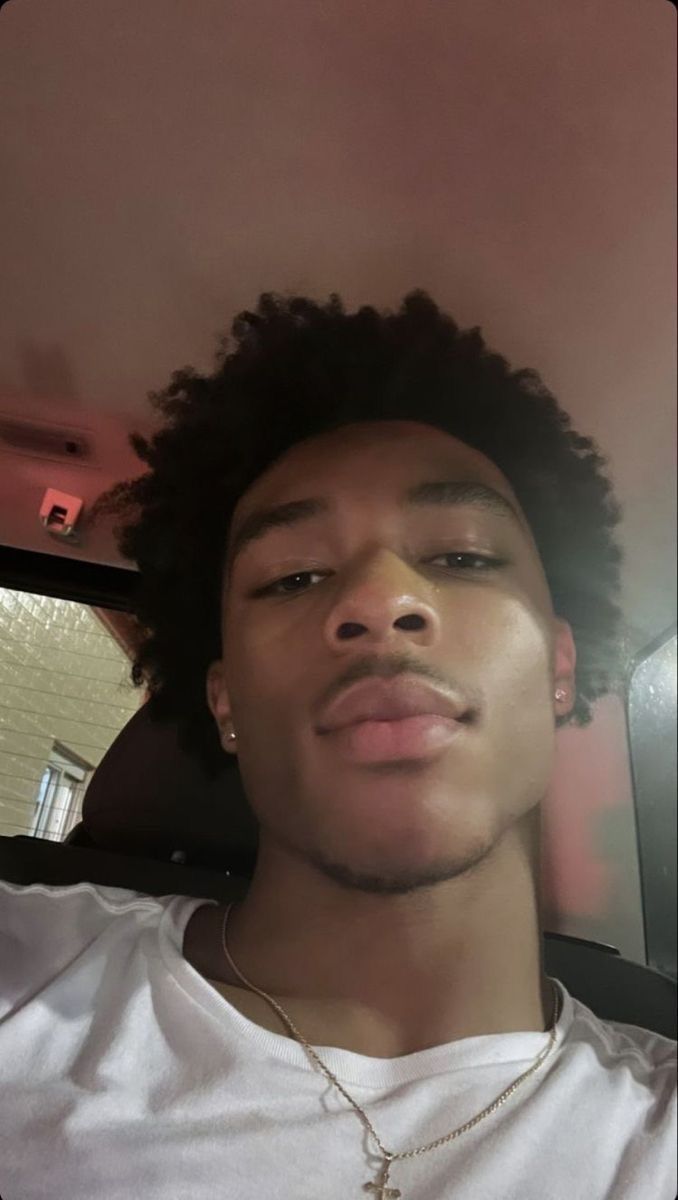 a young man with curly hair wearing a white t - shirt and gold chain necklace