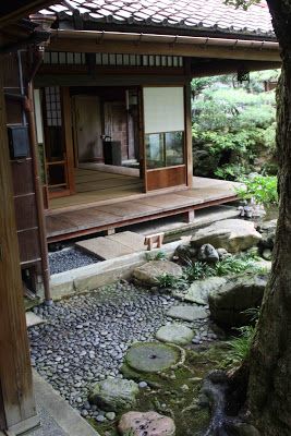 a small japanese house in the middle of a garden with rocks and trees around it