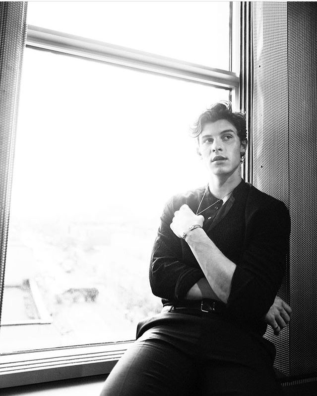 a man sitting on a window sill in front of a window with his arms crossed