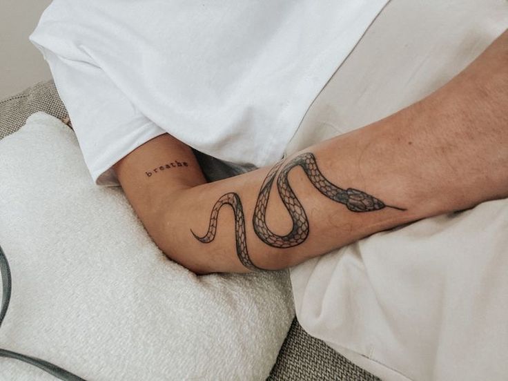 a man with a snake tattoo on his arm laying in bed next to a pillow