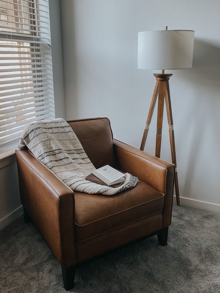 a brown leather chair with a blanket on it in front of a lamp and window