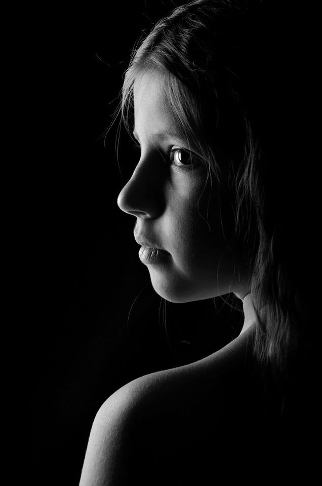 a black and white photo of a woman's face in the dark with her hair pulled back