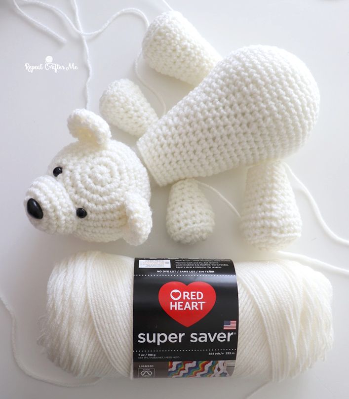 a white crocheted teddy bear laying next to a ball of yarn with the tag red heart super saver on it