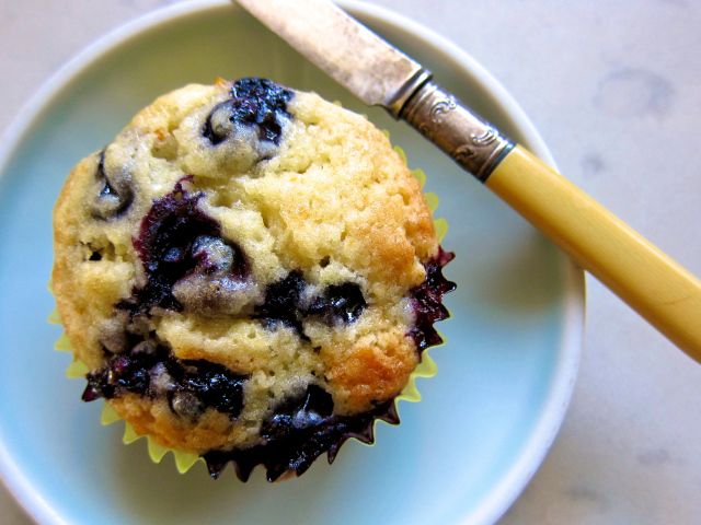 a blueberry muffin sitting on top of a plate next to a wooden spoon