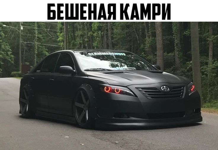 a black car is parked on the street in front of some trees and power lines