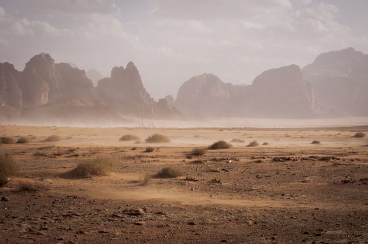 an empty desert with mountains in the background and dust blowing from the ground around it