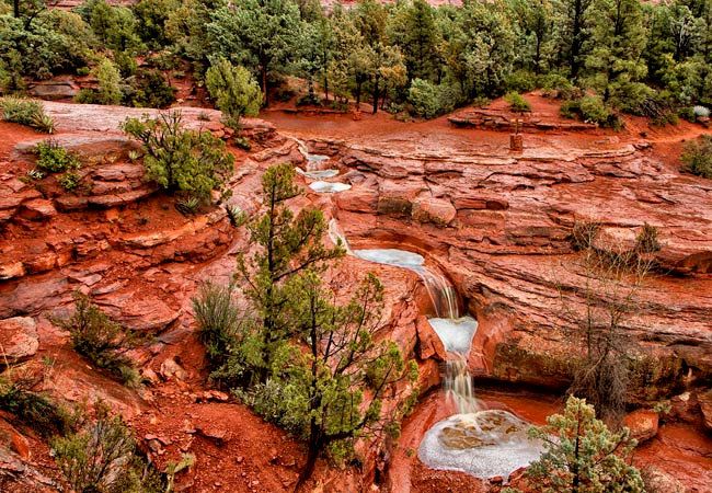 there is a small waterfall in the middle of this rocky area with trees on both sides