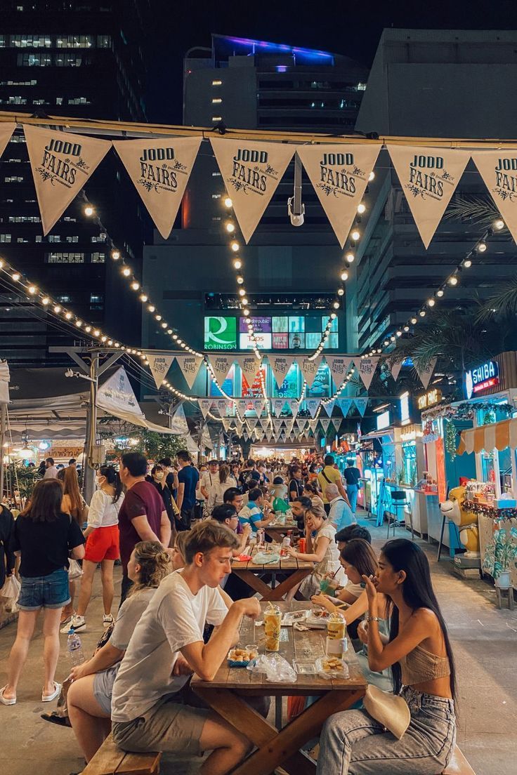 people are sitting at tables in an outdoor market with bunting strung from the ceiling