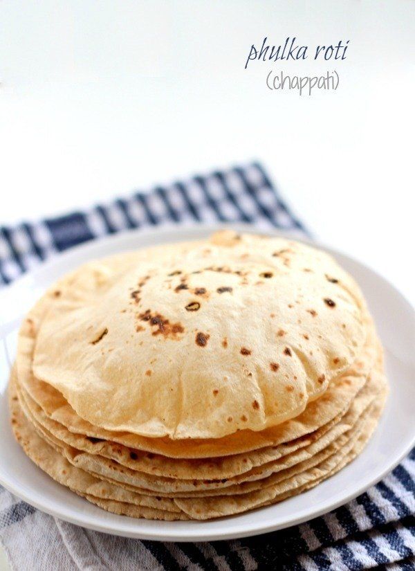 stack of pita bread sitting on top of a white plate next to a blue and white checkered napkin