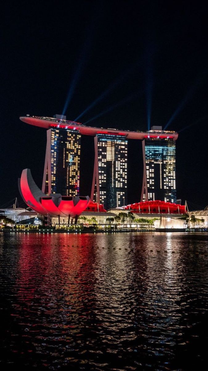 the singapore skyline is lit up at night with bright lights in the sky and reflecting on the water