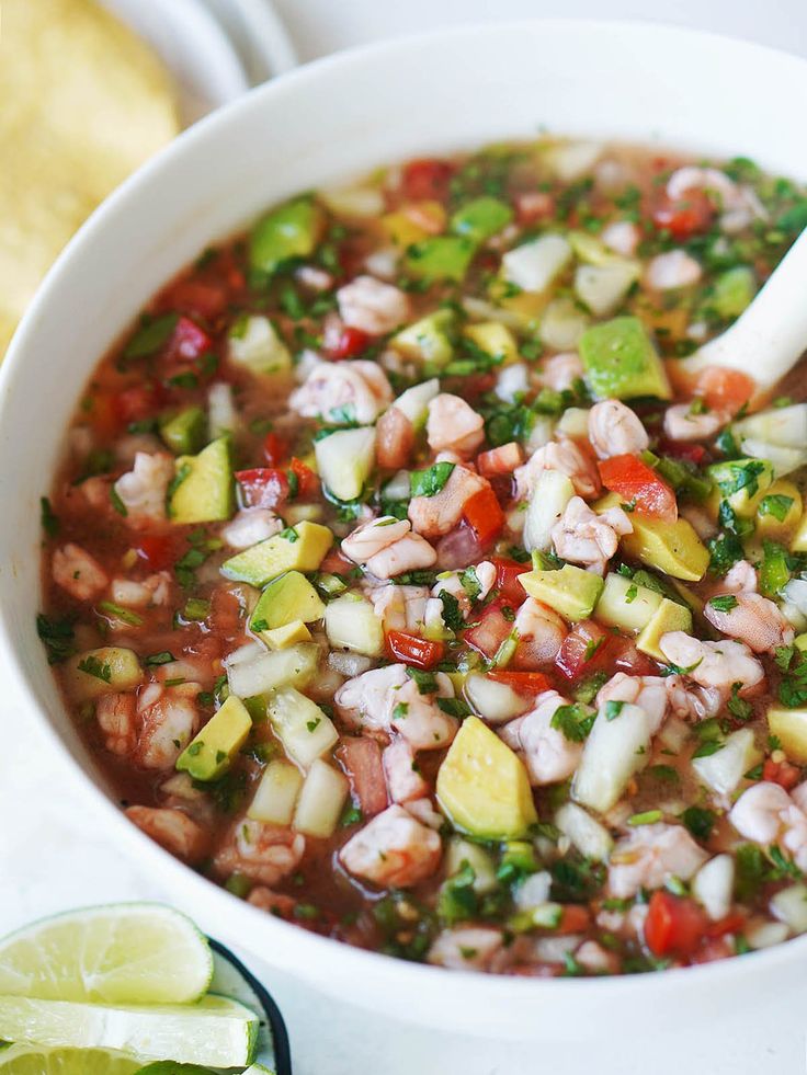 a white bowl filled with vegetable soup next to sliced limes and tortilla chips