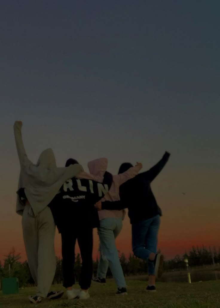 four people standing in the grass with their arms around each other