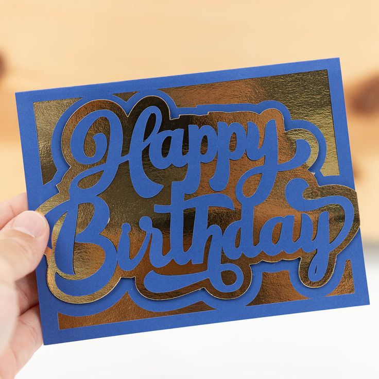 a person holding up a card with the words happy birthday on it in blue and gold