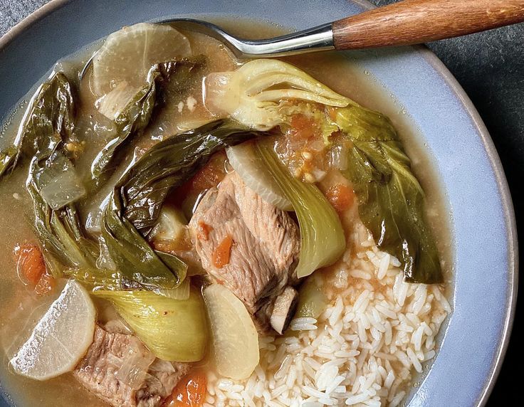 a blue bowl filled with meat and vegetables on top of rice next to a wooden spoon