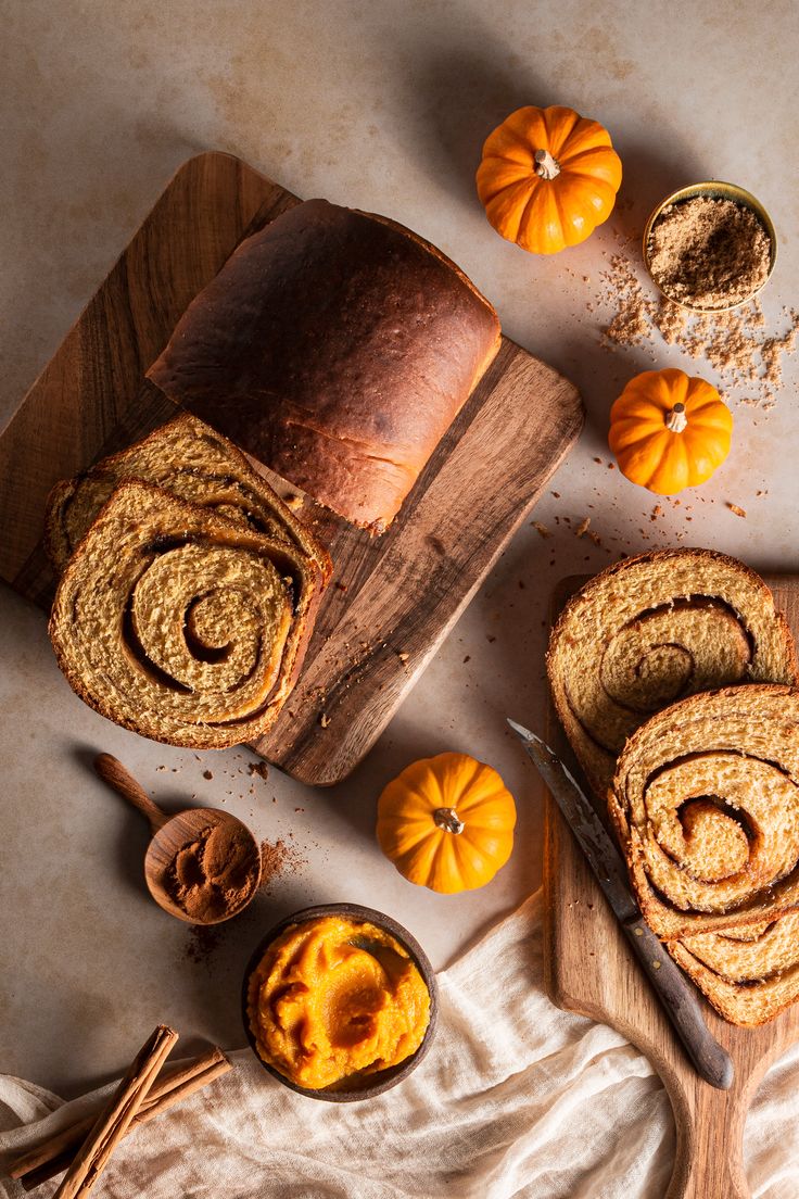 sliced pumpkin bread on a cutting board next to small bowls with cinnamon rolls and mini pumpkins