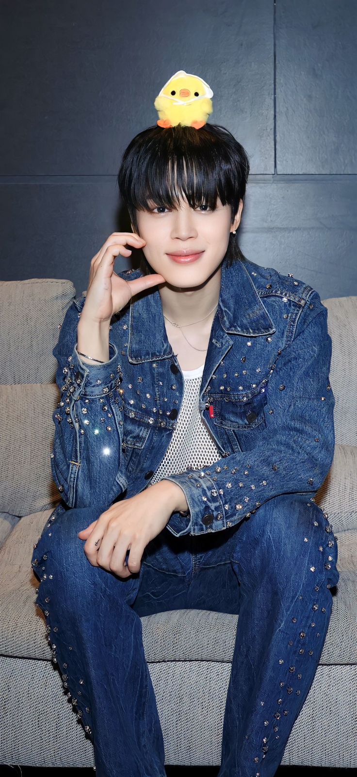 a woman sitting on top of a couch wearing a denim jacket and rubber ducky hat