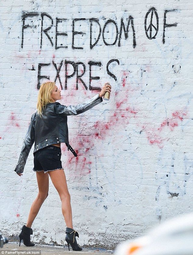 a woman is walking past a wall with graffiti on it and the words freedom express painted on it