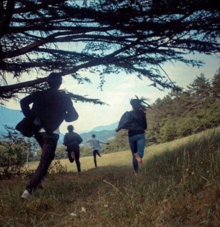 four people are running in the grass near some trees