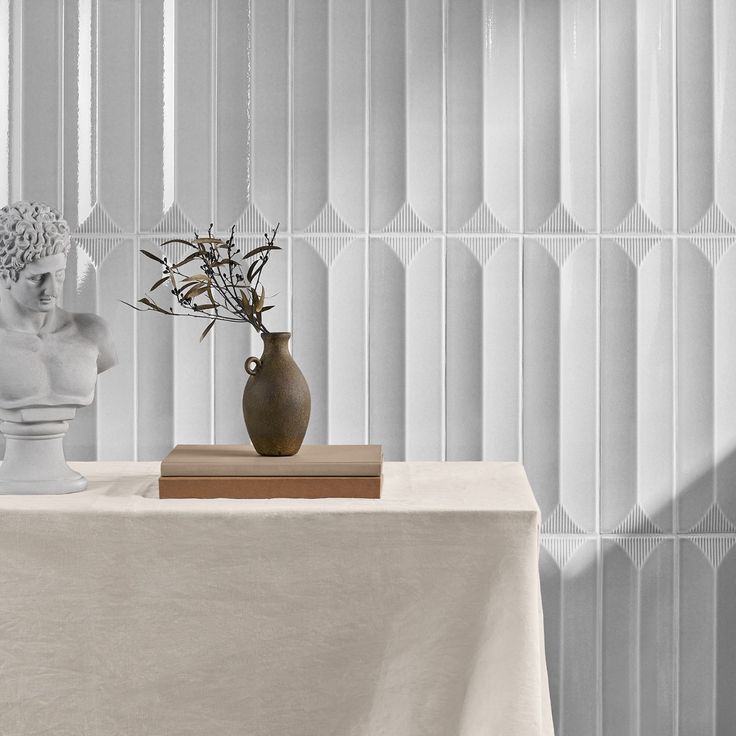 two vases with flowers sit on a table in front of a white tiled wall