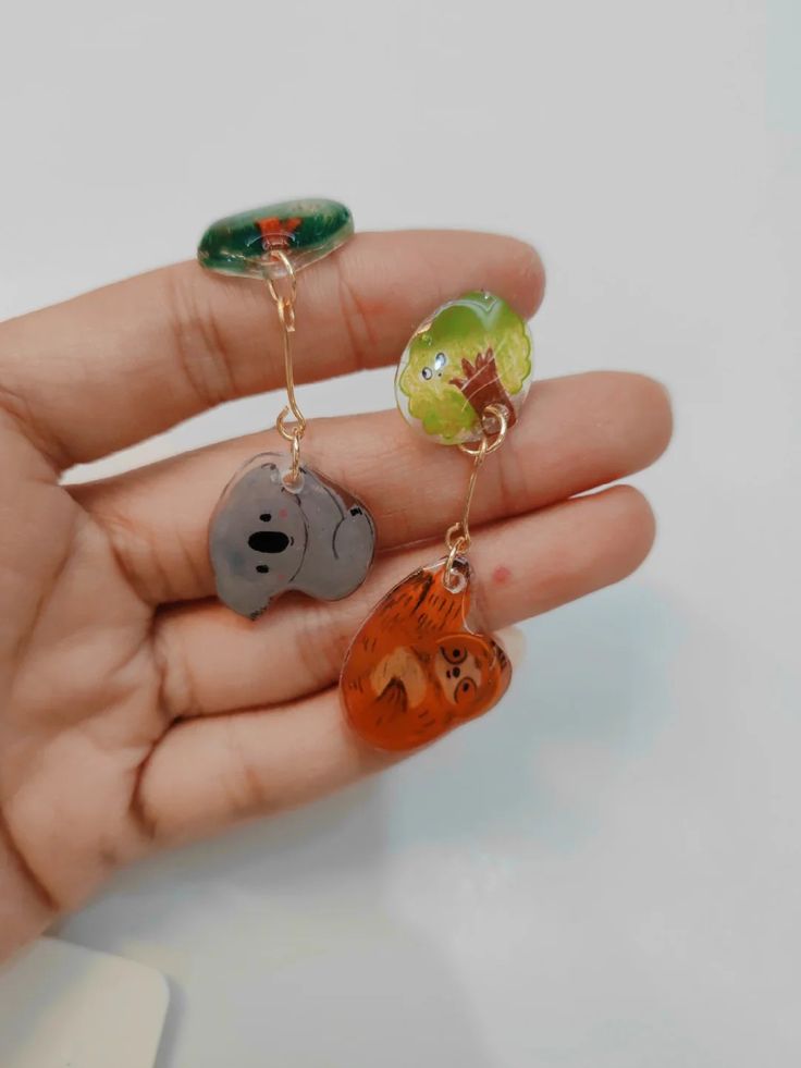 a person is holding three different animal charms in their hand, one with a bear and the other with a bird on it's ear