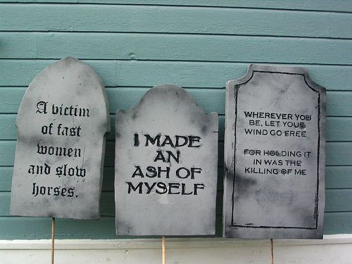 three cement tombstones with writing on them hanging from a line against a blue wall