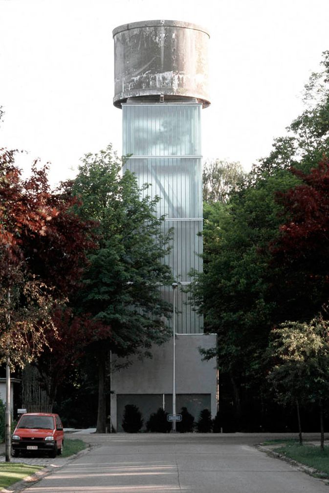 a red car parked in front of a tall building with a water tower on top