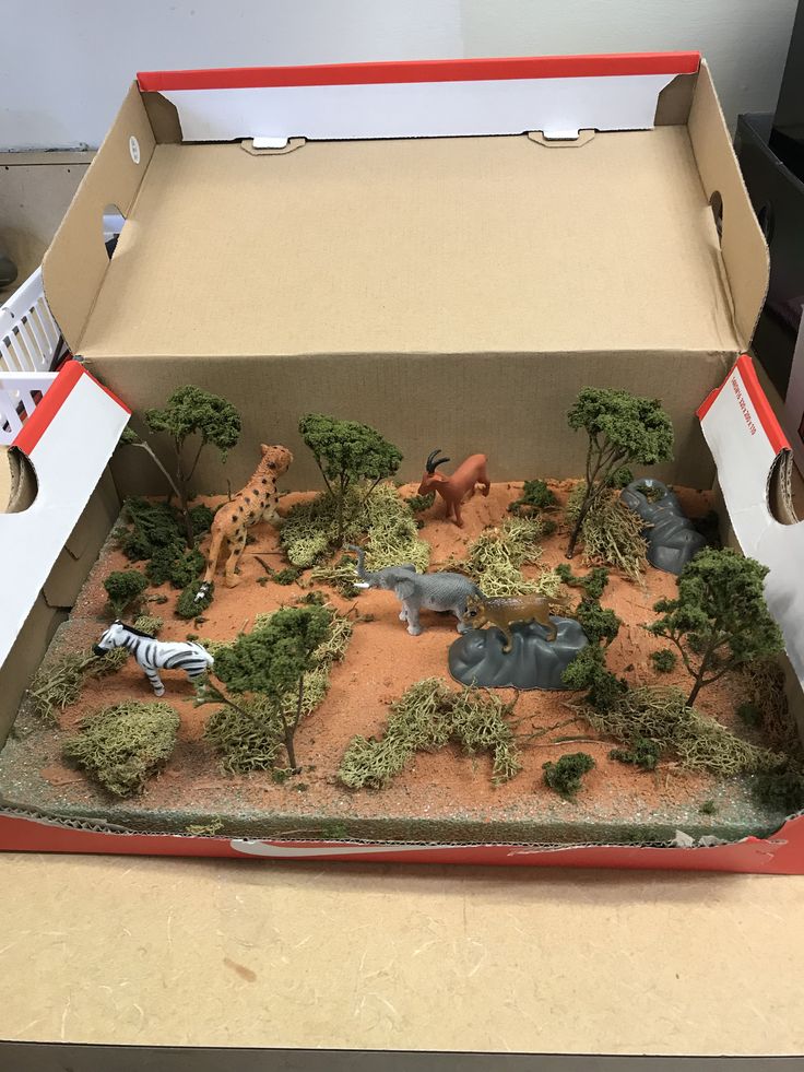 an open cardboard box with toy animals and trees in it on top of a table