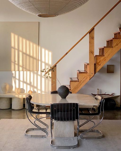 a dining room table with chairs and a vase sitting on it's side in front of a stair case