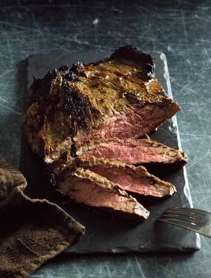 a piece of steak sitting on top of a cutting board next to a knife and fork