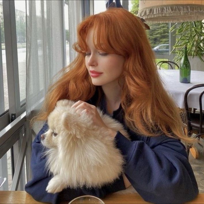 a woman sitting at a table holding a small white dog